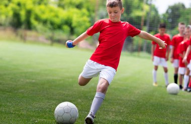 Genç futbolcu büyük çim tarlasında topa vuruyor.