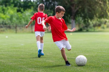 Genç futbolcu büyük çim tarlasında topa vuruyor.