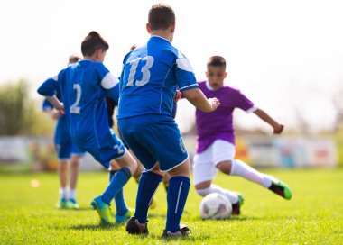 Çocuklar sahada futbol oynuyor.