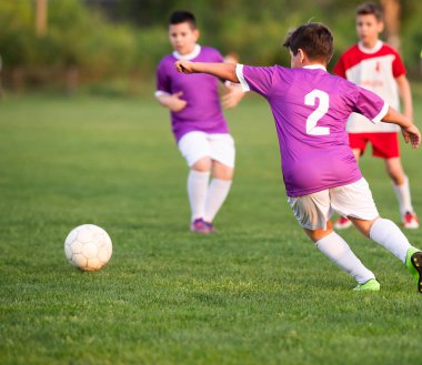 Çocuklar sahada futbol oynuyor.