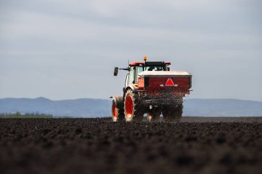 Traktör alana yapay gübre yayıyor.