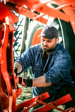 Çiftçi tarladaki tarım makinelerini tamir ediyor. 