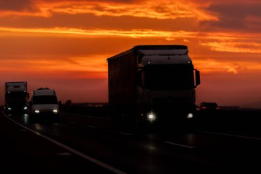 Araba ve kamyon gün batımında otoyolda hareket halinde.