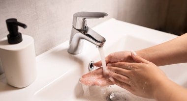 El yıkama. Kadınların elleri suyun altında sabunla ellerini yıkıyor. Gümüş musluklu beyaz lavabo