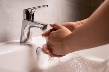 El yıkama. Kadınların elleri suyun altında sabunla ellerini yıkıyor. Gümüş musluklu beyaz lavabo