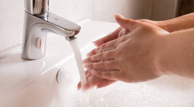 El yıkama. Kadınların elleri suyun altında sabunla ellerini yıkıyor. Gümüş musluklu beyaz lavabo