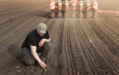 Traktör tarla ekerken genç çiftçi toprağı inceliyor.