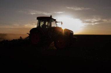 Tractor plowing farm preparing soil for new crop plantation during the evening. clipart