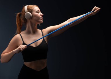 Siyah spor elbiseli bir kadın stüdyoda direniş bandıyla egzersiz yapıyor. Güçlü kaslı vücut için direnç bandı çalışması. Moda Spor Giyim 'deki fitness kızı. Taş Duvara Karşı Eğitim. Aktif Kentliler İçin Yaşam Tarzı Olarak Spor.