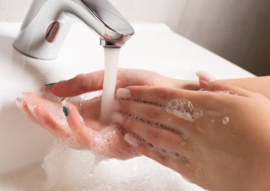 El yıkama. Kadınların elleri suyun altında sabunla ellerini yıkıyor. Gümüş musluklu beyaz lavabo