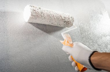 Boyacı el silindiri tutuyor ve beyaz boyalı bir odayı boyuyor.