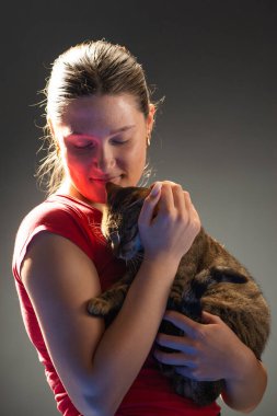 Genç bir kızın portresi siyah bir odada kediye sarılıp oynuyor.