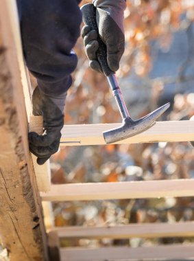 İnşaat işçisi marangoz çatıya çekiçle tahta çakıyor.