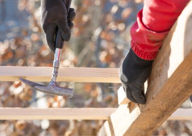 İnşaat işçisi marangoz çatıya çekiçle tahta çakıyor.