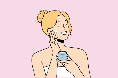 Woman applies anti-aging cream to face to stay beautiful, standing in bath towel after shower. Happy blonde girl smiles and uses cosmetic cream to help prevent wrinkles and pimples. clipart