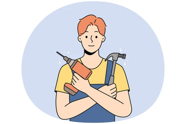 Stock vector Smiling young male mechanic in uniform holding repairing tools in hands. Happy repairman or engineer with drill and hammer ready for fix. Vector illustration.