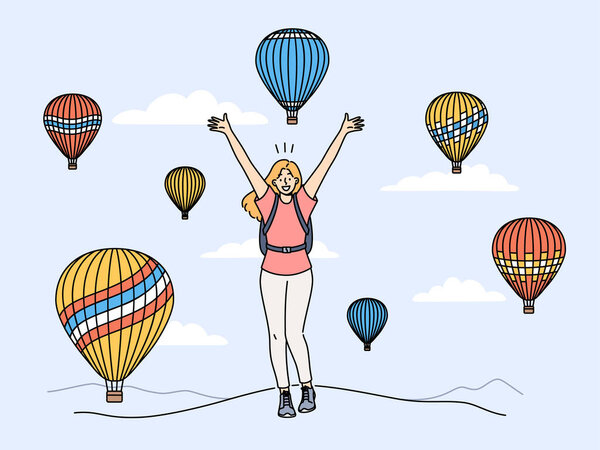 Woman traveler stands among rising balloons and joyfully raises hands up enjoying travel to delightful festival. Concept of travel and getting positive emotions from tours to exotic places