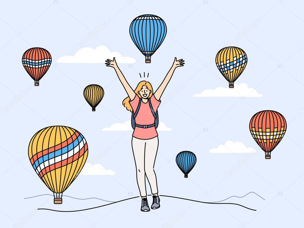 Woman traveler stands among rising balloons and joyfully raises hands up enjoying travel to delightful festival. Concept of travel and getting positive emotions from tours to exotic places