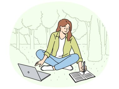 Kadın öğrenci çimenlikte oturup deftere not alıyor ve bilgisayarı kullanarak parkta çalışmaktan keyif alıyor. Eğitim videosu izleyen ve parkta notlar yazan mutlu kız öğrenci.