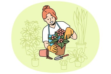 Woman florist takes care of home plants and holds flower pot with blooming violet standing near table. Girl in apron enjoys job as florist, and makes career as salesperson in store or greenhouse clipart