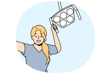 Cerrahi lambalı kadın dişçi gülümsüyor, ameliyathanede duruyor ve hastaya tezahürat yapıyor. Mutlu kız özel klinikte dişçi olarak çalışıyor ve müşterilerin dişlerini tedavi etmesine ve bakıcılardan kurtulmasına yardım ediyor.