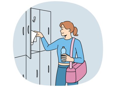 Spor salonuna gelen kadın kişisel eşyaları için dolapların yanında duruyor ve spor antrenmanlarına hazırlanıyor. Spor kıyafetleri için çantası olan bir kız ve formda kalmak için spor salonuna gelen bir şişe su.