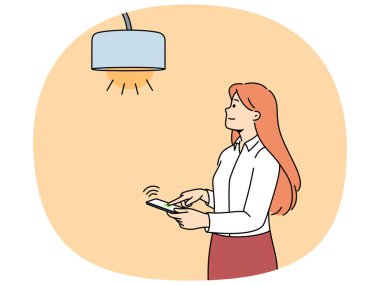 Işığı açmak için cep telefonu ya da akıllı ev uygulaması ile lambayı kontrol eden kadın. Kız akıllı telefona entegre olmuş modern iot teknolojilerini kullanmaktan ve hayatın rahatlığını artırmaktan hoşlanıyor
