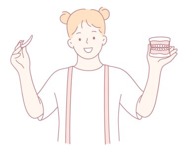 Neşeli bir kız diş fırçasını diş modeliyle tutarak diş temizliği alışkanlıklarını geliştirir.