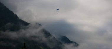 Photo of a sportsman paragliding down among the newfound snow in Trentino Alto Adige on a cloudy, foggy day clipart