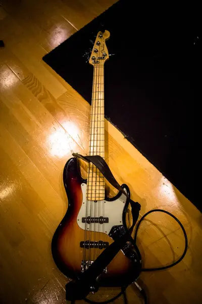 Bir müzik stüdyosunun ahşap zemininde, bir seans molası sırasında uzanan klasik bir caz gitarı.