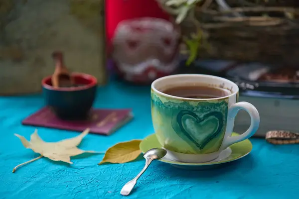 Bahçede çay, baharat, mum ışığı, seyahat kitabı ve sonbahar yapraklı bir turkuaz masa örtüsü.