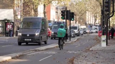 Londra, İngiltere - 2022.12.02: Bir Deliveroo bisikletçisi bisiklet yolunda trafiğin yanındaki yolda