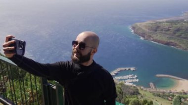 Madeira, Portekiz - 2023.04.04 - 09: Güneşli bir günde arka planda Machiko plajı ile selfie çeken güneş gözlüklü sakallı adam