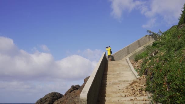 マデイラ ポルトガル 2023 波の卓越性で知られているプラリアダマイアタビーチの写真を撮る黄色いレインコートを着たカメラを持っている男 — ストック動画