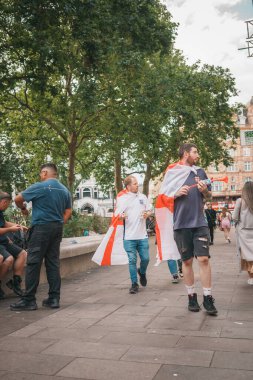Euro Finalleri - Londra - İngiltere - 2024.07.14: Euro Finalleri sırasında İngiltere bayraklarına sarılmış şenlikli futbol taraftarları Londra 'nın merkezinde yürüyor. Canlı atmosfer, spor etkinliğinin heyecanını yakalıyor..