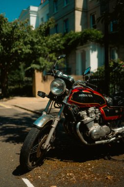 Chiswick, Londra, İngiltere 2025.07.11 Krom detaylı klasik siyah ve kırmızı Honda motosikleti sıcak öğle güneşinde sakin bir yerleşim yerine park edilmiştir..