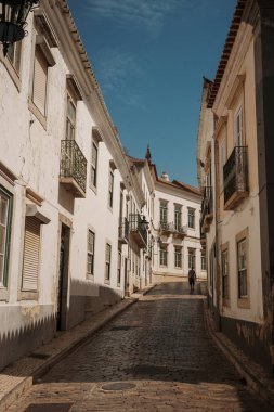 Algarve, Portekiz 2025.06.28 Pembe tişörtlü yaşlı bir adam Algarves 'in göbeğindeki mozaik kaplı bir alışveriş sokağının gölgesinde oturuyor.             