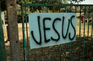 Chiswick, Londra, İngiltere - 2025.08.12 - Parlak yaz güneşinde parkın girişindeki yıpranmış yeşil metal bir kapıya sprey boyayla boyanmış İsa tabelası.