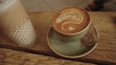 Sagres, Algarve, Portekiz 2025.07.01 Karışık latte sanatıyla bir cappuccino manzarası ve ahşap bir kafeteryada buzlu latte.. 