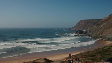 Algarve, Portekiz 2025.07.01 Güçlü Atlantik Okyanusu dalgaları Praia da Arrifana kıyılarına doğru akar ve kıyı şeridi üzerinde dramatik kayalık kayalıklar yükselir.. 