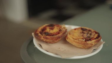 Praia da Luz, Algarve, Portekiz 2025.07.01 İki geleneksel Portekiz pastel de nata kremalı turtasının yakın çekimi beyaz bir tabakta peçeteyle servis ediliyor.. 