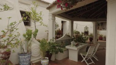 Algarve, Portekiz 2025.07.01 Deniz kızı tasarımlı fayanslı bir bank, küçük bir çeşme, saksı bitkileri ve kırsal ahşap çatı kirişleri içeren büyüleyici bir Akdeniz tarzı avlu.. 