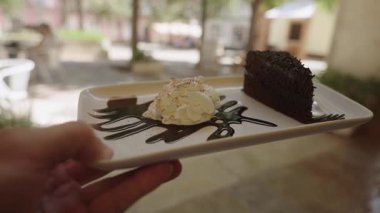 Portekiz 2025.07.01 Bir tatlı tabağının yakın çekimi Bir dilim çikolatalı pasta, üzerine tarçın sürülmüş krema, ve çikolata şurubu serpiştirilmiş, 