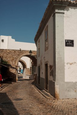 Algarve, Portekiz 2025.06.28 Taş kemerlere doğru kıvrılan dar bir kaldırım taşı caddesi ve güneşli bir günde beyazlatılmış binalar.. 
