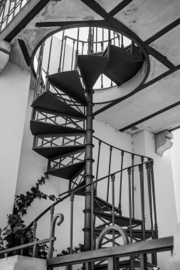 Algarve, Portekiz 2025.06.28 dekoratif metal spiral merdiven, süslü parmaklıklar ile yan tarafında sarmaşık büyüyen pastel duvarlar karşı kurulmuş. 