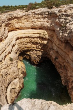 Algarve, Portekiz 2025.06.29 Doğal bir deniz mağarasına dramatik bir dikey bakış, katmanlı kireçtaşı kaya duvarları ve berrak bir yaz gökyüzü altında canlı turkuaz Atlantik sularını gösteriyor.. 