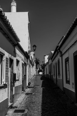 Algarve, Portekiz 2025.06.30 derin mavi bir gökyüzü altında renkli geleneksel evlerle kaplı küçük bir kaldırım taşı caddesi.. 