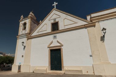 Algarve, Portekiz 2025.06.30 'da Portekiz' in büyüleyici bir kasabasında, koyu mavi bir gökyüzünün altında, çan kulesi, haçı ve koyu yeşil kapıları olan, tarihi bir kilise kuruldu.. 