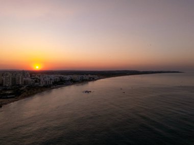Portimo, Algarve, Portekiz 2025.07.01: Güneşin doğuşuyla Praia da Rocha 'nın çarpıcı hava manzarası, şehrin ufuk çizgisinde yükselen altın güneş ve sakin Atlantik suları. 