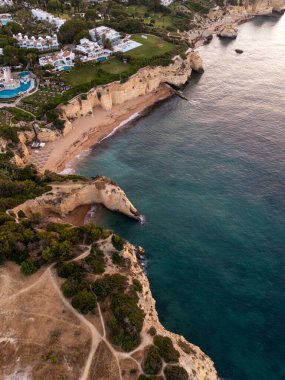 Algarve, Portekiz 2025.07.01: Gözlerden uzak bir plajın şafağındaki insansız hava aracı manzarası altın uçurumlar, turkuaz sular ve Atlantik Okyanusu 'na bakan havuzları olan lüks villalar ile çevrilidir.. 